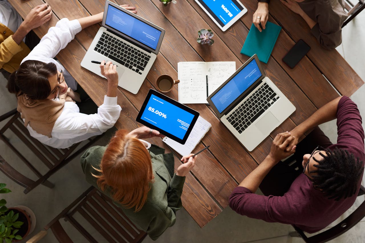 why-choose-us Diverse team discussing business strategies with laptops and tablets at a wooden table.